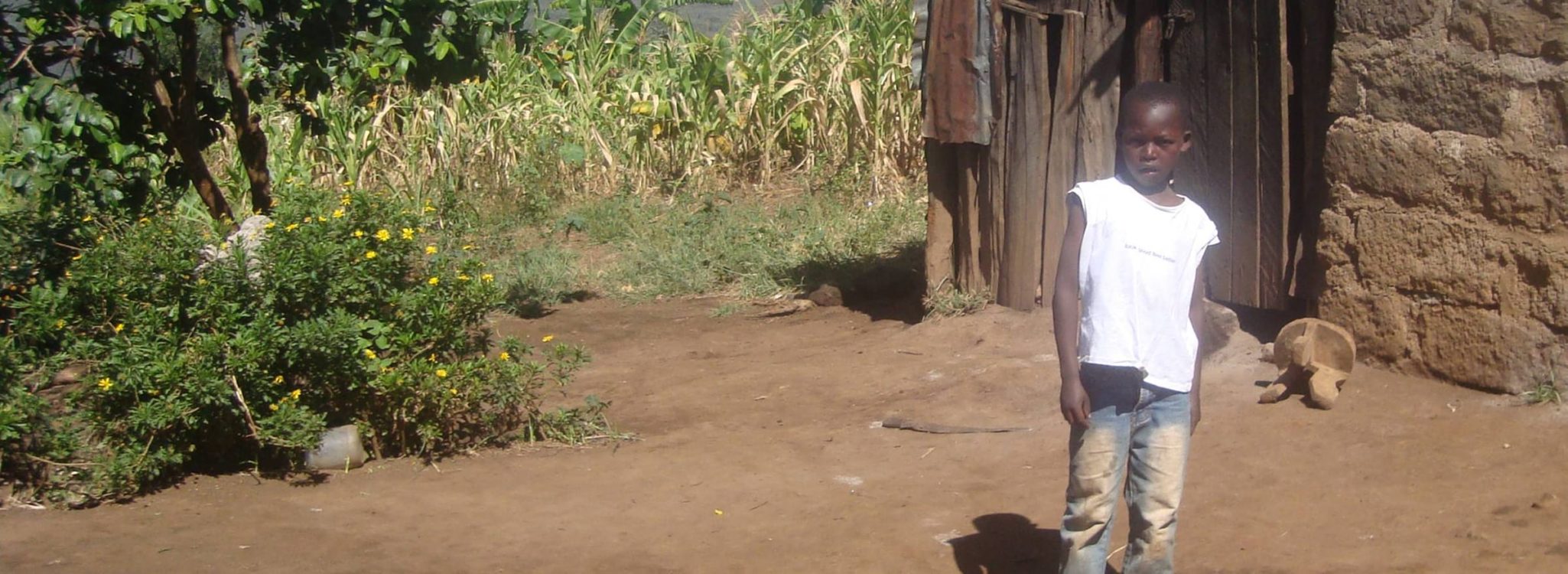 Kenyan child in white t-shirt standing outside a rural building